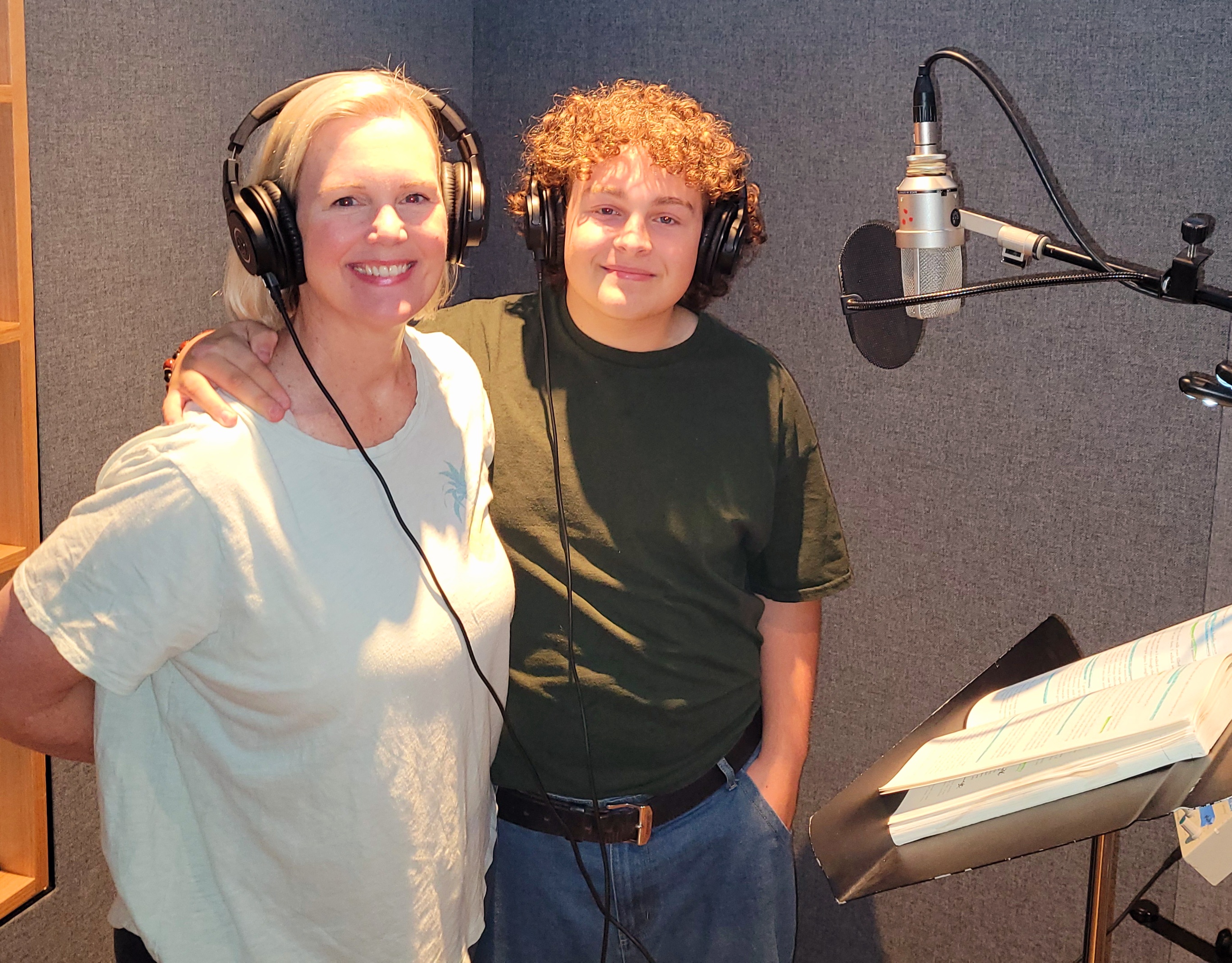 Shannon and Jerry wearing headphones and smiling beside a studio microphone, with an open, marked-up book on the music stand.